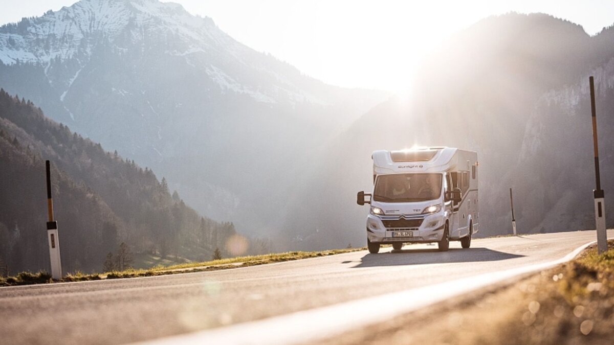Untersichtiger Schuss auf ein weißes Sunlight Wohnmobil auf einer Gebirgsstraße mit Gegenlicht der Sonne.