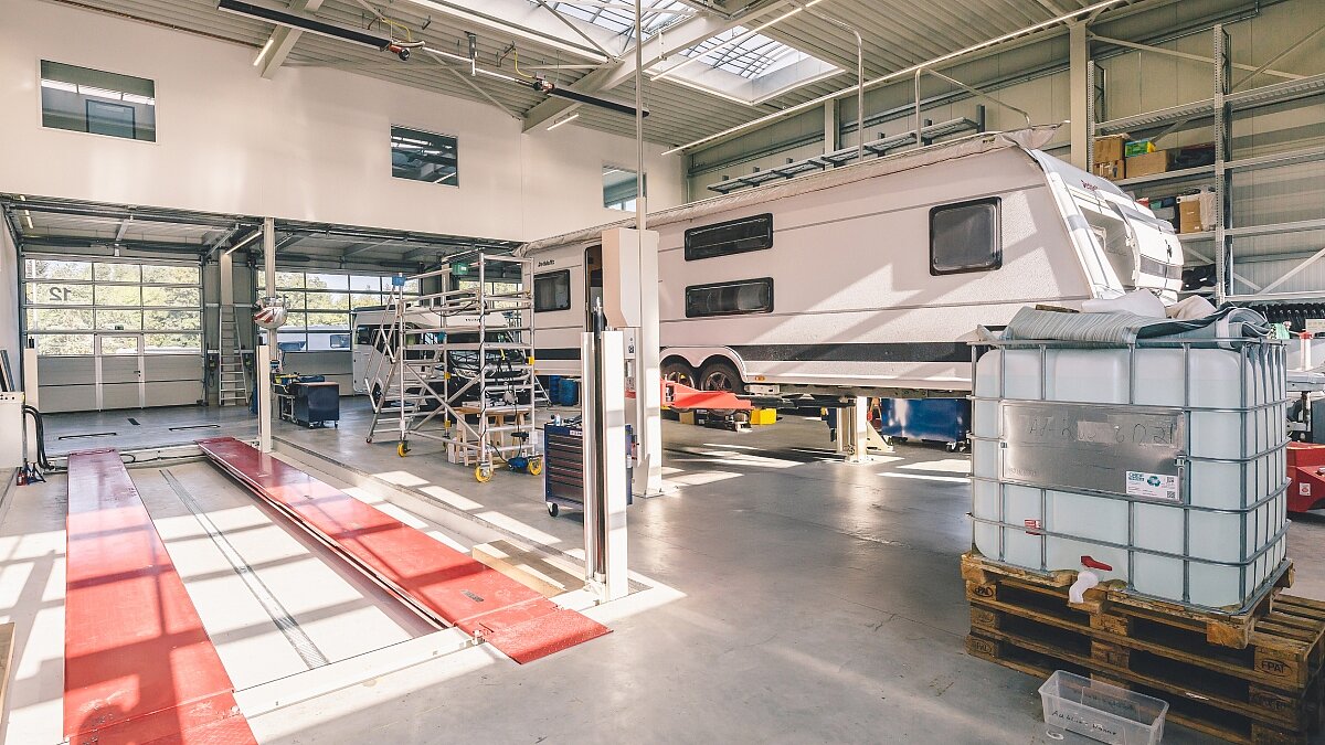 Bild aus der sonnen-durchfluteten Werkstatt von Ullrich Caravaning mit Blick auf eine leere Hebebühne sowie einen Wohnwagen und ein Wohnmobil.