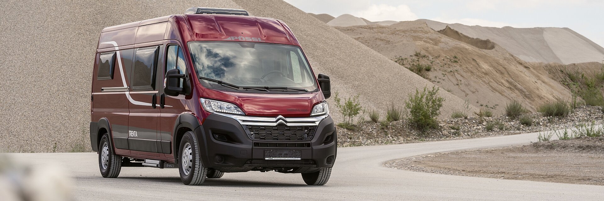 Roter Pössl Campervan auf einer steinigen Straße.