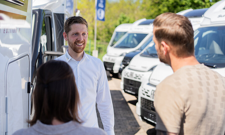 Beratungsgespräch zur Vermietung von Wohnmobilen auf dem Hof von Ullrich Caravanging zwischen ein Pärchen und einem Verkaufsberater..